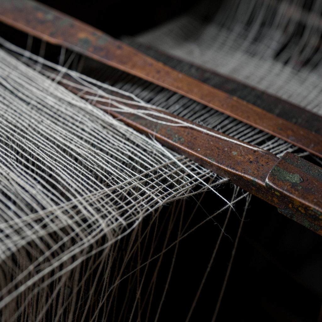 Close view of warp threads on a loom with a few broken strands beside a copper reed
